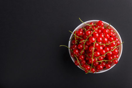 Fresh red currant in white bowl on black background. top view, flat lay, copy space.