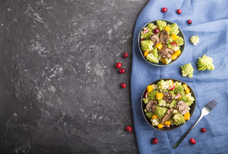 Vegetarian salad from romanesco cabbage, champignons, cranberry, avocado and pumpkin on a black...