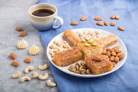 traditional arabic sweets (basbus, kunafa, baklava), a cup of coffee and nuts on a gray concrete background and blue textile. side view, close up.の写真素材