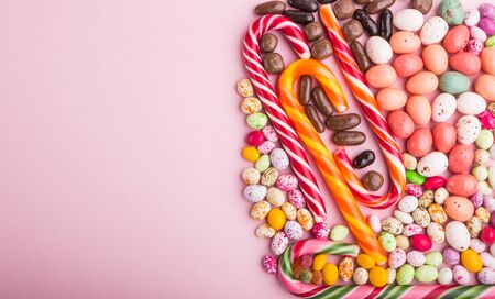 Colorful multicolored candies on a pink pastel background. Christmas cane, chocolate eggs, caramel dragees. copy space, top view, flat lay.の写真素材