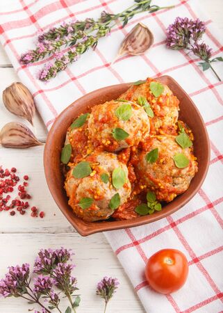Pork meatballs with tomato sauce, oregano leaves, spices and herbs in clay bowl on a white wooden background with linen textile. side view, close upの写真素材