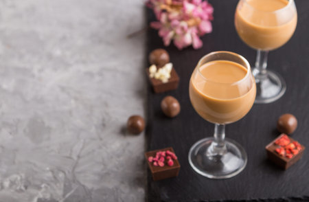 Sweet chocolate liqueur in glass with chocolate candies on a gray concrete background and black...