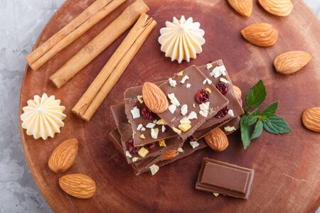 A pieces of milk chocolate with almonds and dried fruits on a brown wooden board on a gray concrete background. top view, close up, selective focus, flat lay.の写真素材