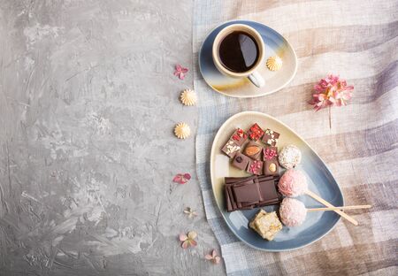 A pieces of homemade chocolate with coconut candies and a cup of coffee on a gray concreteの写真素材