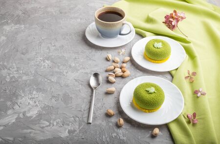 Green mousse cake with pistachio cream and a cup of coffee on a gray concrete background and green textile. side view, copy space.の写真素材