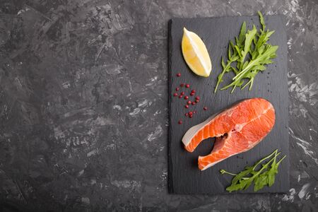 Raw salmon steak with arugula and lemon on a black slate board on a black concreteの写真素材