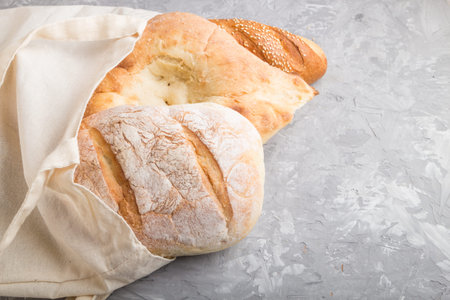 Reusable textile grocery bag with fresh baked bread on a gray concrete background. side view, copy...