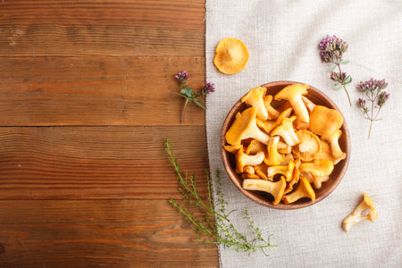 Chanterelle mushrooms in wooden bowl and spice herbs on wooden background with linen textile. top view, copy space, flat lay.の写真素材