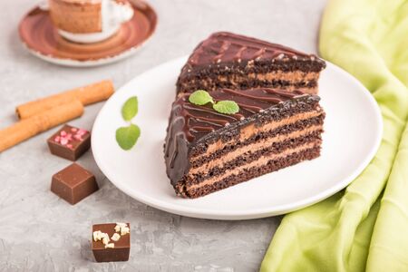Homemade chocolate cake with milk cream and a cup of coffee on a gray concrete background with green textile. side view, close up, selective focus.の写真素材