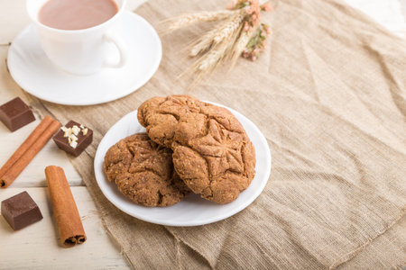 homemade oatmeal cookies with a cup of cocoa on a linen textile and white wooden background. side...