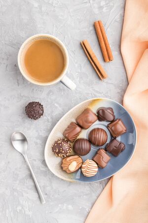 Different chocolate candies and a cup of coffee on a gray concrete background and orange textile. top view, flat lay, close up.の写真素材