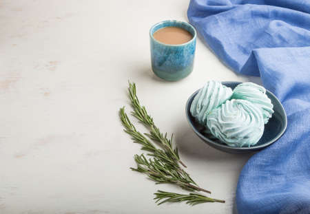 Blue colored homemade zephyr or marshmallow with cup of coffee on white wooden background with blue textile. side view, close up, copy space.の写真素材