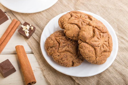 homemade oatmeal cookies with a cup of cocoa on a linen textile and white wooden background. side...