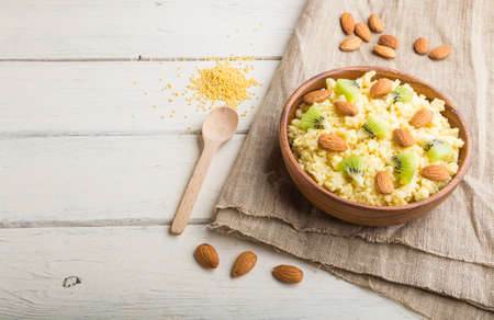 Millet porridge with kiwi and almonds in wooden bowl on a white wooden background and linen textile. Side view, copy space.の写真素材