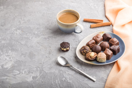 Different chocolate candies and a cup of coffee on a gray concrete background and orange textile....