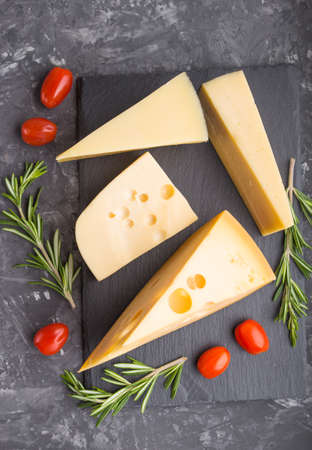 Various types of cheese with rosemary and tomatoes on black slate board on a black concrete background. Top view, flat lay, close up.の写真素材