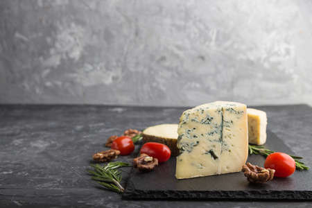 Blue cheese and various types of cheese with rosemary and tomatoes on black slate board on a black concrete background. Side view, copy space, selective focus.の写真素材