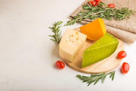 Green basil cheese and various types of cheese with rosemary and tomatoes on wooden board on a white...