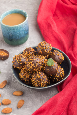 Chocolate caramel ball candies with almonds and a cup of coffee on a gray concrete background and...