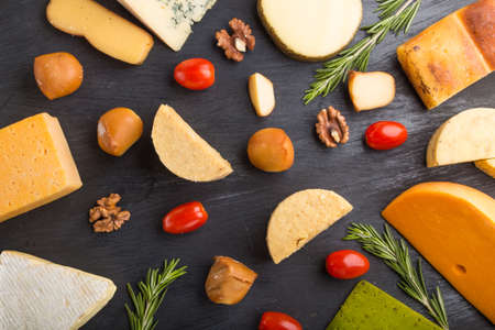 Set of different types of cheese with rosemary and tomatoes on a black wooden background. Top view, flat lay, close up.の写真素材