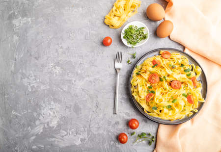 Reginelle semolina pasta with tomato, eggs and microgreen sprouts on a gray concrete background and orange textile. Top view, flat lay, copy space.の写真素材