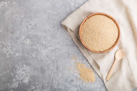 Wooden bowl with raw white quinoa seeds and wooden spoon on a gray concrete background and linen textile. Top view, flat lay, copy space.の写真素材