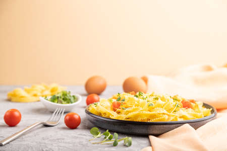 Reginelle semolina pasta with tomato, eggs and microgreen sprouts on a gray and orange background and orange textile. Side view, selective focus.の写真素材