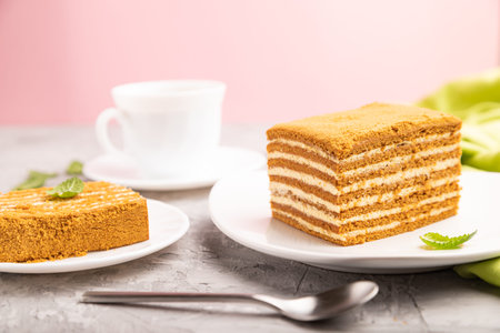 Homemade honey cake with milk cream and mint with cup of coffee on a and pink background and green...