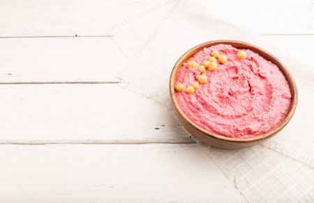 Hummus with beet in wooden bowl on a white wooden background and linen textile. Side view, copy space.の写真素材