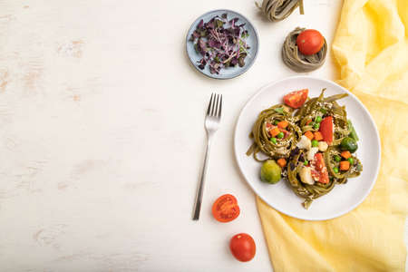 Tagliatelle green spinach pasta with tomato, pea and microgreen sprouts on a white wooden background and yellow textile. Top view, flat lay, copy space.の写真素材