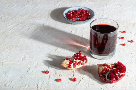 Glass of pomegranate juice on a white concrete background. Hard light, contrast. Side view, copy...