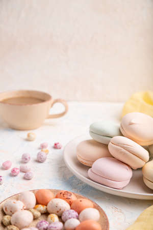 Colored zephyr or marshmallow with cup of coffee and dragees on white concrete background and yellow textile. Side view, copy space, selective focus.の写真素材