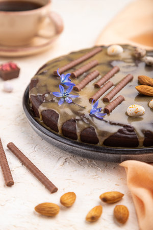 Homemade chocolate brownie cake with caramel cream and almonds with cup of coffee on a white...