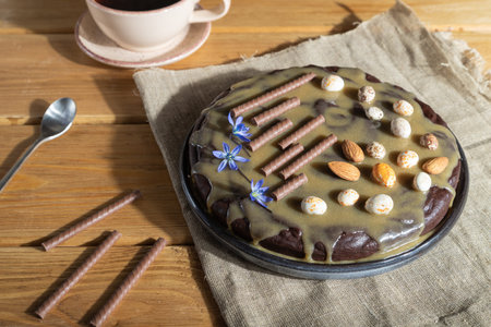 Homemade chocolate brownie cake with caramel cream and almonds with cup of coffee on wooden...