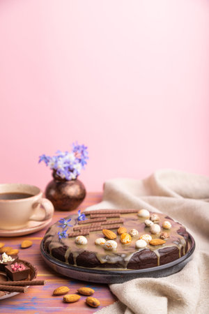 Homemade chocolate brownie cake with caramel cream and almonds with cup of coffee on a colored and pink background and linen textile. Side view, copy space, selective focus.の写真素材