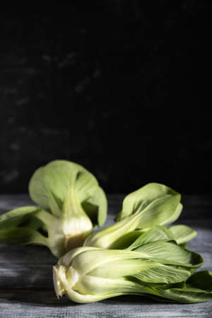 Fresh green bok choy or pac choi chinese cabbage on a gray wooden background. Hard light, contrast, dark, moody. Side view, copy space, selective focus.の写真素材