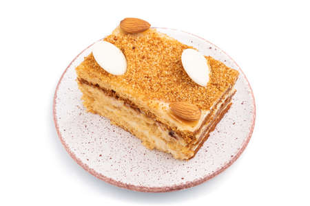 Honey cake with milk cream, caramel, almonds isolated on a white background. Side view, close up.の写真素材