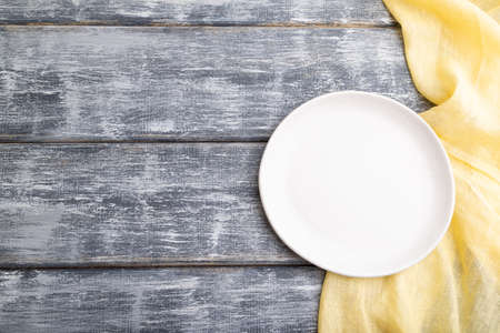 Empty white ceramic plate on gray wooden background and yellow linen textile. Top view, copy space, flat lay.の写真素材