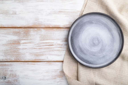 Empty gray ceramic plate on white wooden background and linen textile. Top view, copy space, flat lay.の写真素材