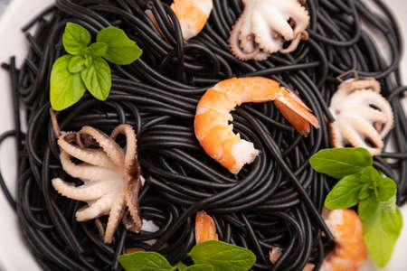 Black cuttlefish ink pasta with shrimps or prawns and small octopuses on gray wooden background and blue textile. Top view, close up, selective focus.の写真素材