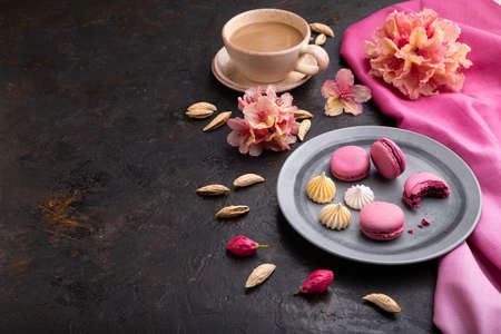 Purple macarons or macaroons cakes with cup of coffee on a black concrete background and pink textile. Side view, copy space.の写真素材