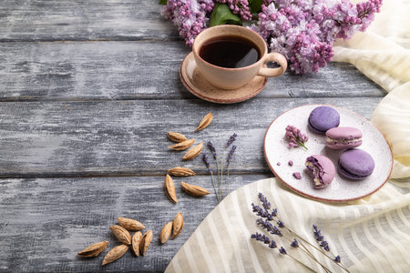 Purple macarons or macaroons cakes with cup of coffee on a gray wooden background and white linen...