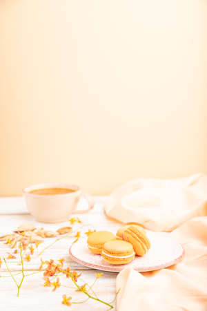 Orange macarons or macaroons cakes with cup of apricot juice on a white wooden background and orange linen textile. Side view, copy space, selective focus.の写真素材