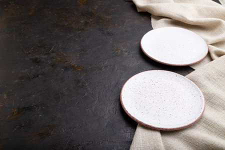 Two empty white plates on black concrete background and linen textile. Side view, copy space.