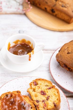 Homemade cake with raisins, almonds, soft caramel and a cup of coffee on a white wooden background....