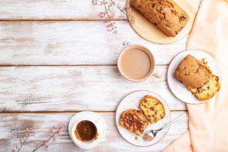 Homemade cake with raisins, almonds, soft caramel and a cup of coffee on a white wooden background...