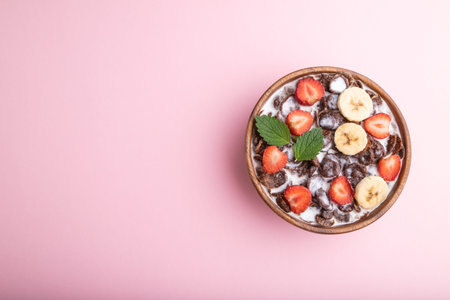 Chocolate cornflakes with milk and strawberry in wooden bowl on pink pastel background. Top view,...