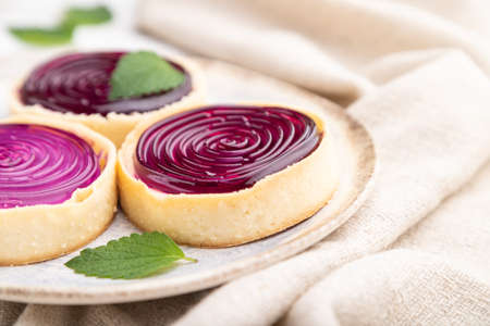 Sweet tartlets with jelly and milk cream with cup of coffee on a white wooden background and linen textile. Side view, close up, selective focus.の写真素材