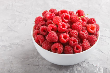 Fresh raspberry in white bowl on gray concrete background. side view, close up.