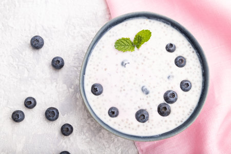 Yogurt with blueberry in ceramic bowl on gray concrete background and pink linen textile. top view,...